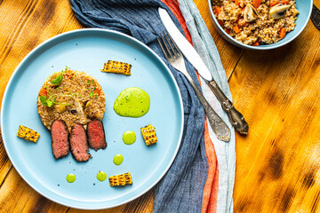 Sliced filet mignon steak with grits, mushrooms and corn served on a blue plate with a napkin and...