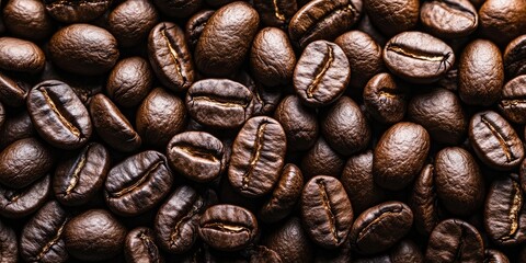 Fototapeta premium Richly textured assortment of dark roasted coffee beans in varying shades of brown fills the frame, creating a warm inviting background.