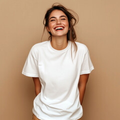 Laughing young woman model with messy hairstyle, dressed in white oversized t-shirt standing near plain background, studio shot. Blank short sleeve tee template. Women crewneck basic tshirt mock up