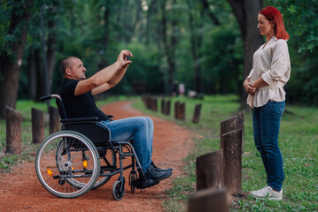 Man in wheelchair taking photo of pregnant woman in park