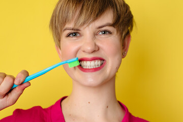A young Caucasian woman with an amazing smile with a toothbrush in her hands on a yellow isolated background.