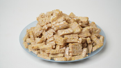 Raw tempeh cut into squares on a blue plate isolated on a white background.