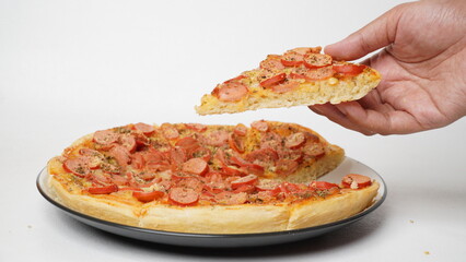 Side view of one hand pulling pizza from a pizza pan with beef sausage topping served on a white round plate and placed on a table with a white background.