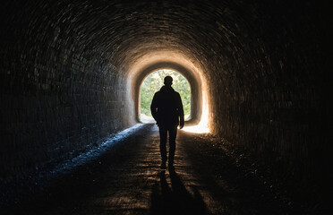 Person walking towards a light at the end of a dark tunnel, representing hope