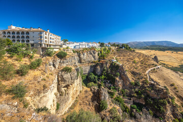 Fototapeta premium Ronda town in Spain. White village perched on dramatic cliffs, overlooking a vast, dry landscape under a clear blue sky.