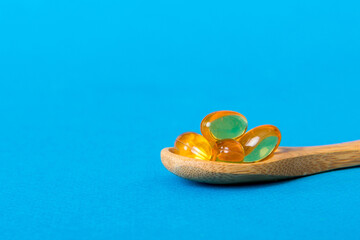 Vitamin omega capsules in a spoon on a colored background. Pills served as a healthy meal. Red soft...