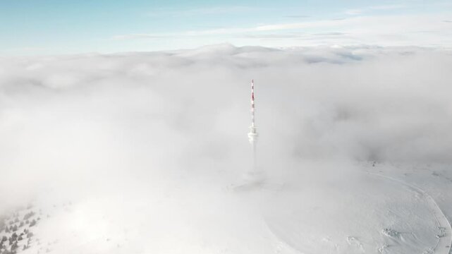 Drone slow approach to Praded iconic tower atop Jesen&iacute;k mountains, framed by mist and fog in daylight, transmitter and receiver tower above hotel