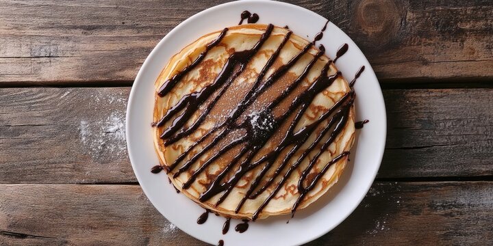 Stack of fluffy pancakes drizzled with chocolate syrup on a white plate positioned center on rustic wooden background with scattered flour