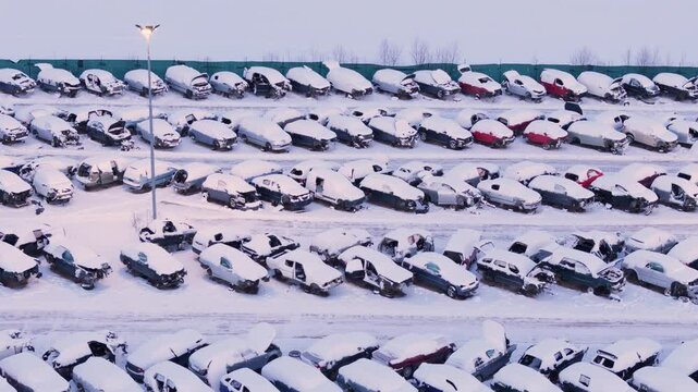 Broken down wrecked vehicles at scrap yard covered in winter snow, aerial view