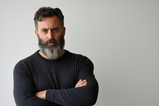 Portrait of a mature man with graying beard and crossed arms, conveying seriousness and disapproval against a white background