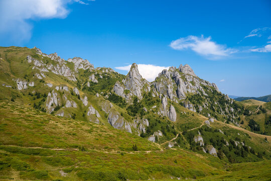 Rocky Landscape Covered With Green Grass, Crossed By A Mountain Path, Blue Sky With Clouds In The Background