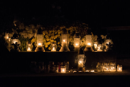 A Bunch Of Grave Candles Glowing With A Yellow Light On A Gravestone On All Saints' Day In The Night