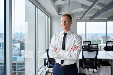 Serious young professional business man, confident executive ceo manager, rich male investor wearing tie standing crossing arms in office looking away through skyscraper window thinking of future.