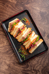 A delicious sandwich stacked with layers of fresh vegetables and savory fillings, served on a black plate. Perfect for appetizing food photography and culinary presentations.