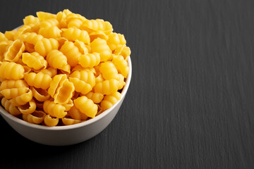 Homemade Dry Raw Gnocchi Pasta in a Bowl on a black background, side view. Copy space.