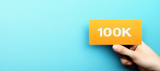 Hand Holding a Card Indicating 100k Subscribers, Followers, or Digital Success on Blue Background