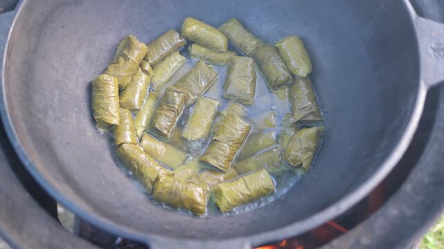Vegetables, grape leaves stuffed with minced meat, are boiled and stewed in a cauldron and steam goes over them