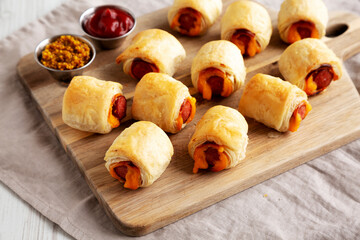 Homemade Pigs in a Blanket with Ketchup and Mustard on a Wooden Board, side view.