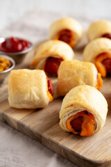 Homemade Pigs in a Blanket with Ketchup and Mustard on a Wooden Board, side view. Close-up.