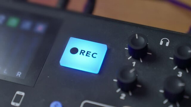 Hand pressing on REC button to begin recording and then clicking again to stop audio session. Sound and audio console detail or close up. Engineer or podcast host in home or professional sound studio