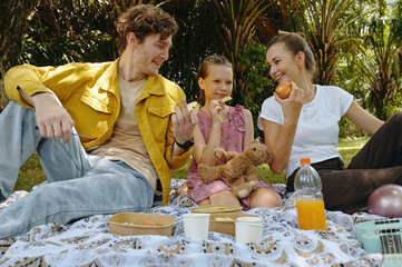 Family of three having snack and drinking juice while having picnic in the park