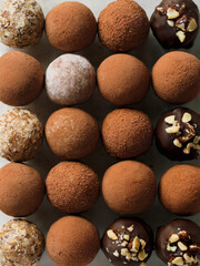 A collection of round truffles or dessert balls arranged in a grid pattern on a white background. The truffles vary in size and are coated with different textures and toppings