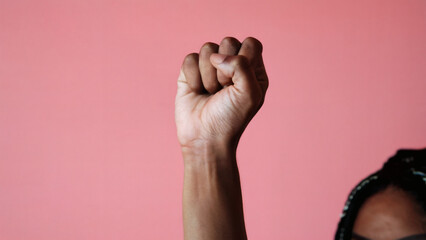 international women's day: A striking close-up of a woman's raised fist positioned to the right side of the frame against a solid pink background, symbolizing strength, unity, and empowerment