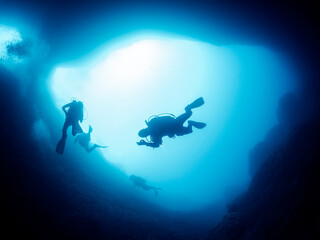 silhouette of unrecognizable scuba diver doing ok symbol with hand while swimming in dark cave undersea in deep clear water, concept of active leisure and underwater adventure