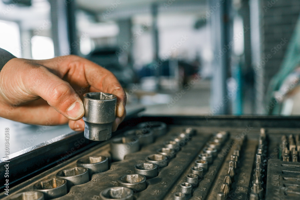Poster hand selecting a metal socket wrench piece from an organized tool tray in a workshop setting, symbol
