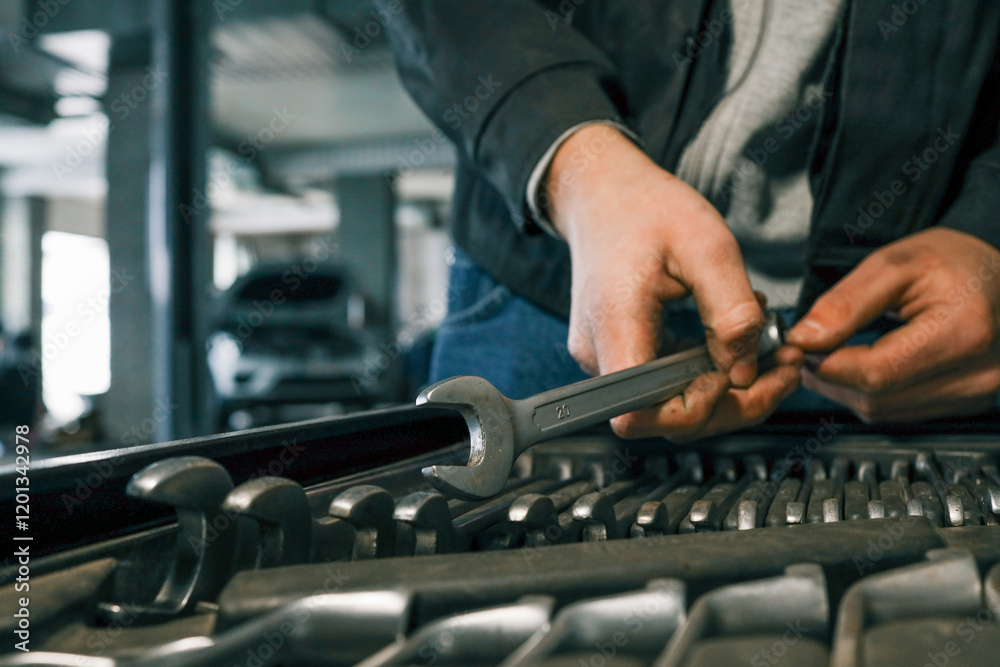 Poster Close-up of a mechanic's hand picking wrenches from a well-organized tool tray in a workshop. Metal wrenches in various sizes, ready for repair tasks