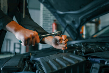 Close-up of a mechanic's hands using a wrench to perform maintenance on a car engine in a workshop setting
