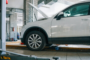 White car with an open hood in an auto repair shop. Vehicle on a car lift for maintenance and inspection in a professional garage