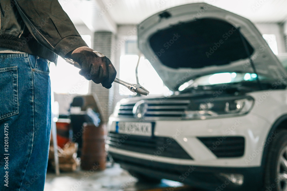 Poster mechanic holding an adjustable wrench in a workshop. a white car with its hood open is visible in th