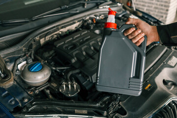 Close-up of a mechanic holding a bottle of motor oil and an oil dipstick, performing an oil change in a vehicle. Highlights car maintenance and servicing tasks