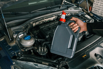 Fototapeta premium Close-up of a mechanic holding a bottle of motor oil and an oil dipstick, performing an oil change in a vehicle. Highlights car maintenance and servicing tasks
