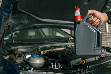 Close-up of a mechanic holding a bottle of motor oil and an oil dipstick, performing an oil change in a vehicle. Highlights car maintenance and servicing tasks