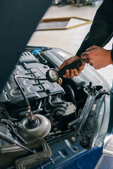 Fototapeta premium Mechanic using a pressure gauge to test and diagnose the engine system of a car in a workshop. Open hood reveals components and testing equipment