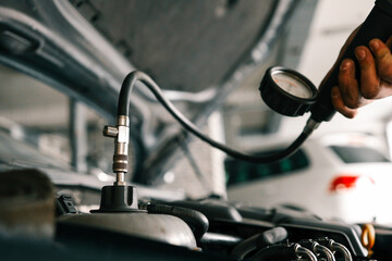 Mechanic using a pressure gauge to test and diagnose the engine system of a car in a workshop. Open hood reveals components and testing equipment