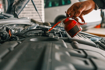 Mechanic using a red oil can to lubricate a vehicle's engine components during routine maintenance in a workshop
