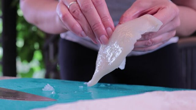 Squid on a cutting board slicing, women's hands cleaning and slicing squid carcasses, cooking seafood