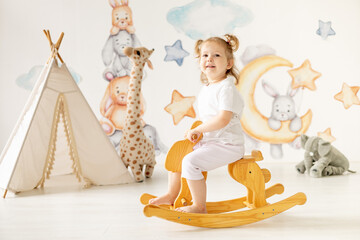 little child girl blonde plays in the children's room swinging on a wooden horse, children's leisure, kindergarten