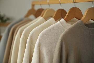 Obraz premium Neutral-colored sweaters on wooden hangers in a minimalist setting