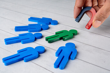 A magnet is pick up a green figure from a group of blue figures. Recruitment, talent acquisition, standing out from the crowd concept.