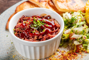 A vibrant plate featuring crispy flatbreads, tender pulled meat in sauce, fresh salad, and grilled corn, all beautifully arranged on a textured platter against a wooden background.
