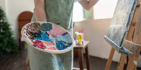 Focused artist presenting a colorful palette while preparing to paint on canvas in a light filled studio