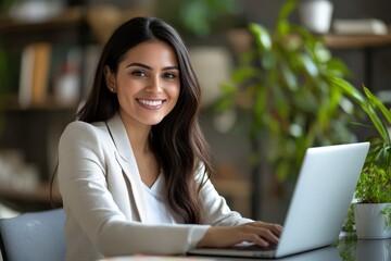 A busy young female executive working on her laptop in the office. A smiling Hispanic businesswoman, employed by the company, sits at her work desk, serving as a professional HR manager while focusing