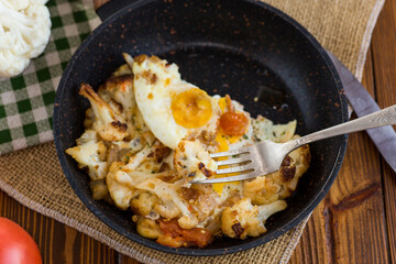 fried omelette with cauliflower and vegetables in a frying pan on a wooden table