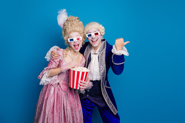 Joyful couple in baroque costumes enjoying 3D movie experience against a vibrant blue backdrop