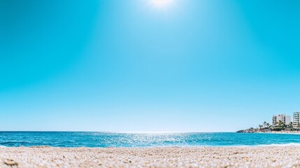 Sunny beach under clear blue sky with sparkling ocean waves and distant shoreline buildings, vibrant summer atmosphere