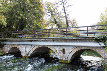 Fototapeta premium The Crni Drim River flows under a stone bridge with three arches, creating a picturesque scene as it merges with the serene waters of Lake Ohrid.